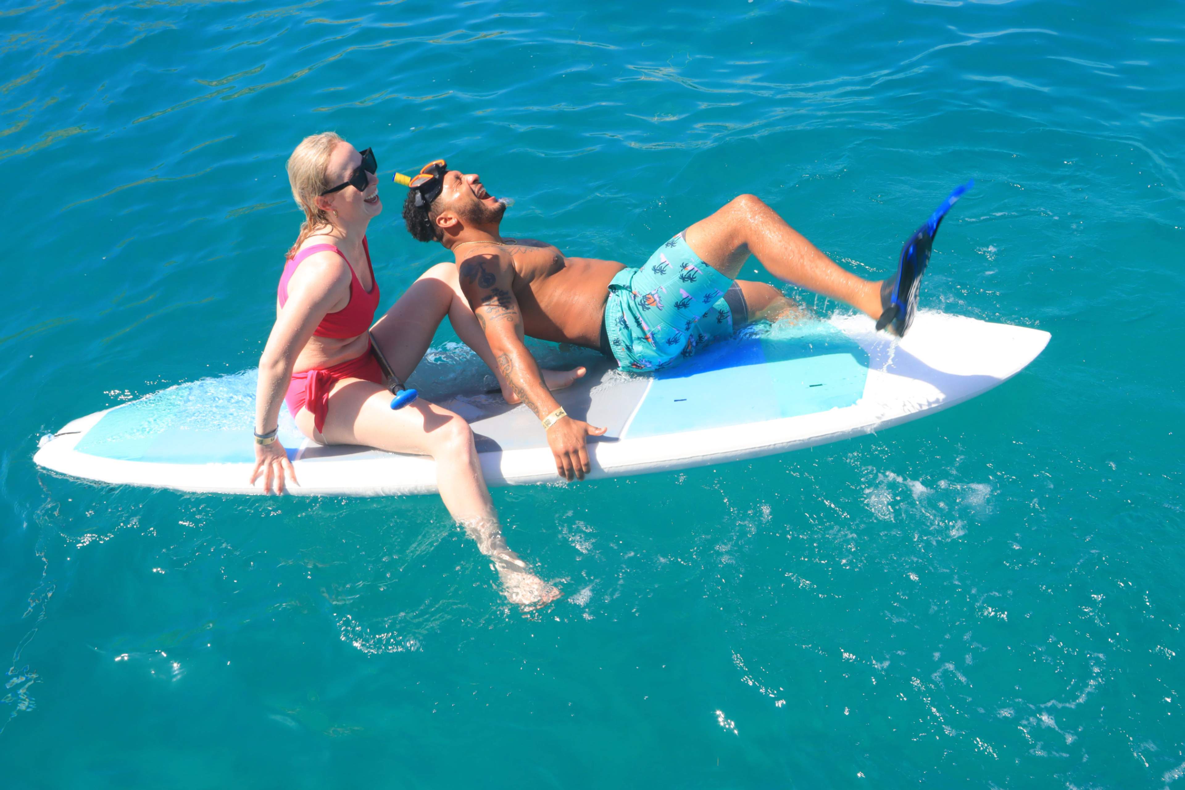 two people are enjoying the water while relaxing on a surfboard in a clear blue sea.