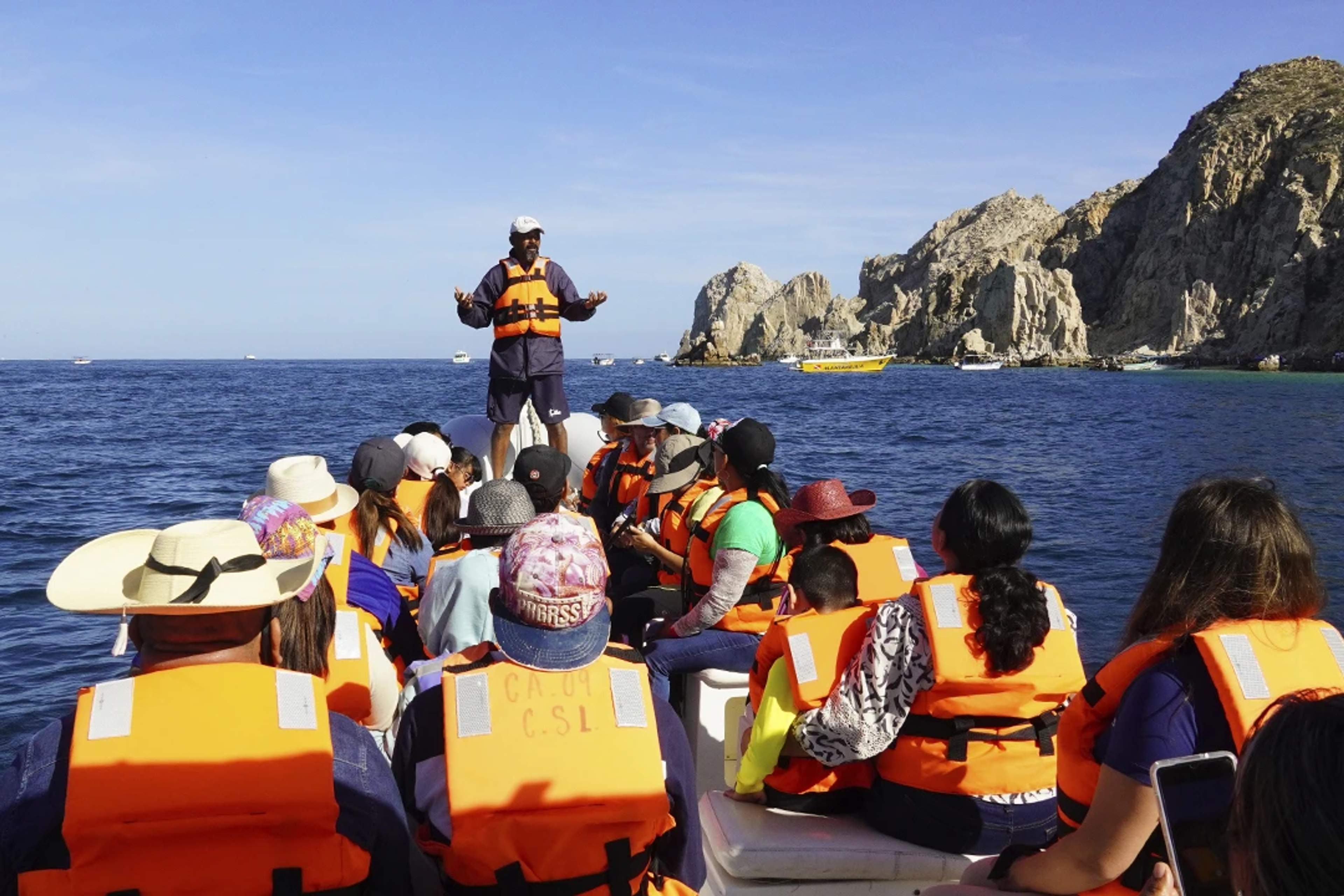 A Cabo Adventures guide explains marine life and the environment to a group of people on a boat.