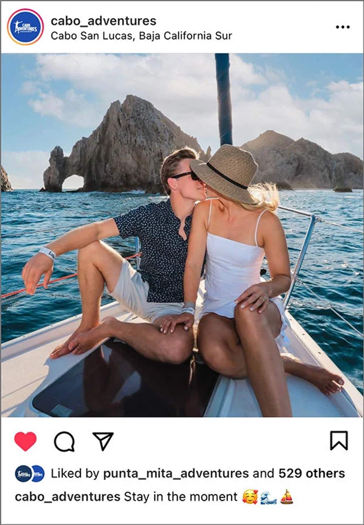 Couple kissing on a boat with the Arch of Cabo San Lucas in the background.