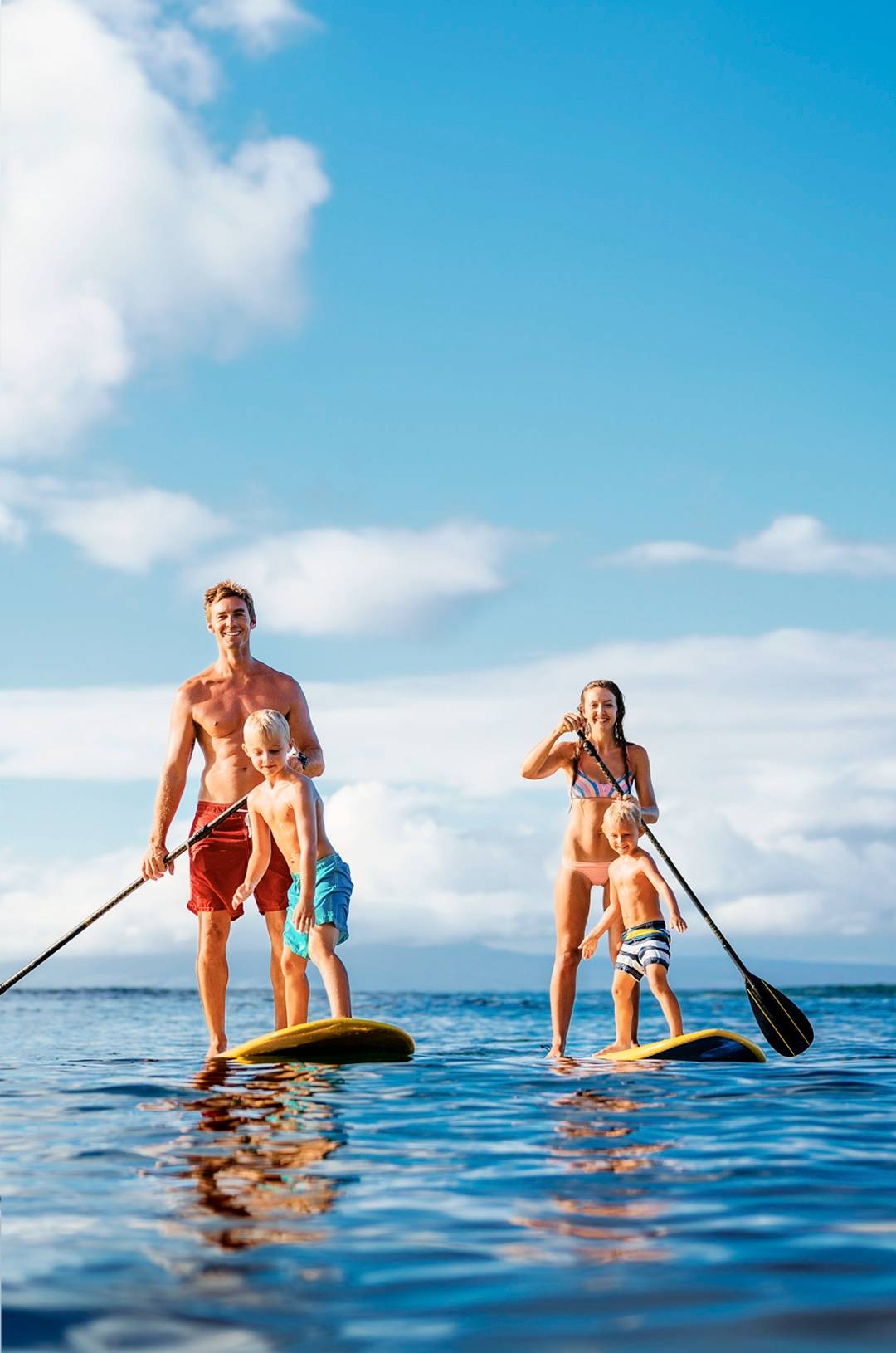 A family paddleboarding on the ocean, with a father and child on one board and a mother and child on another.