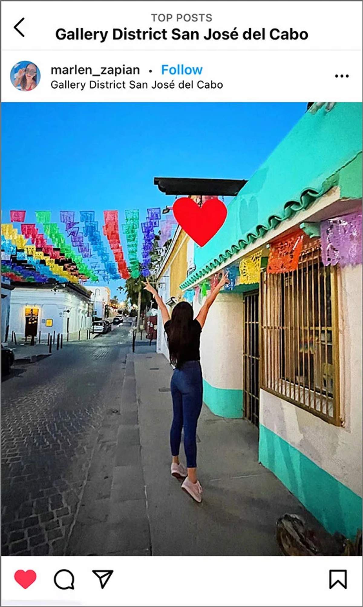 Woman with arms raised in the colorful Gallery District of San José del Cabo, decorated with vibrant flags.