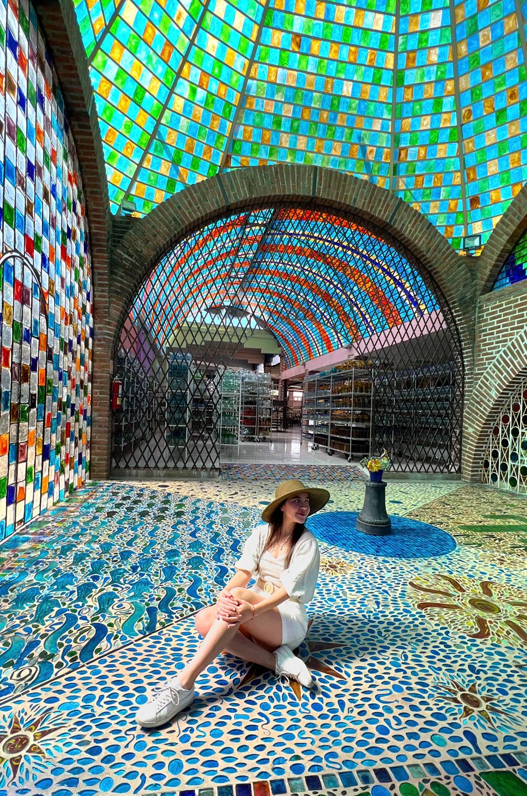 Woman sitting on a colorful mosaic floor under a vibrant stained glass dome.