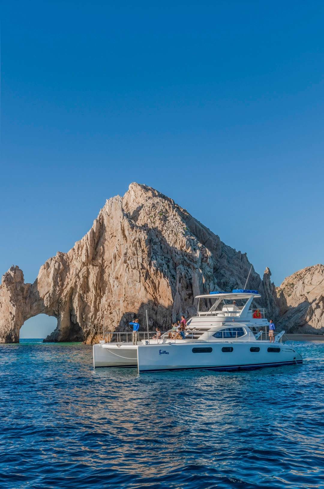 A catamaran with tourists sails near the famous arch rock formation in Cabo San Lucas.