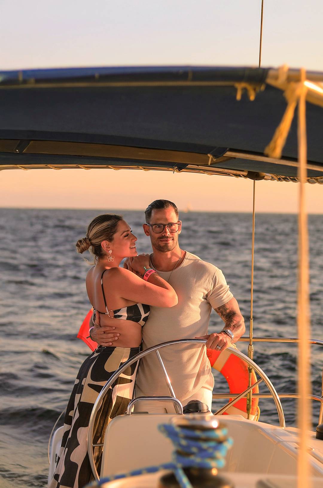 A couple embraces at the helm of a sailboat, enjoying a romantic sunset cruise on the open sea.