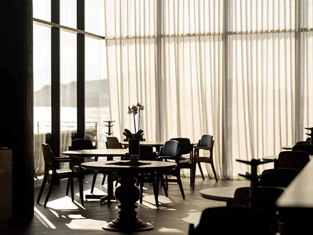 A serene, sunlit dining room with elegant decor and large windows offering a view of the ocean, creating a tranquil and sophisticated atmosphere.