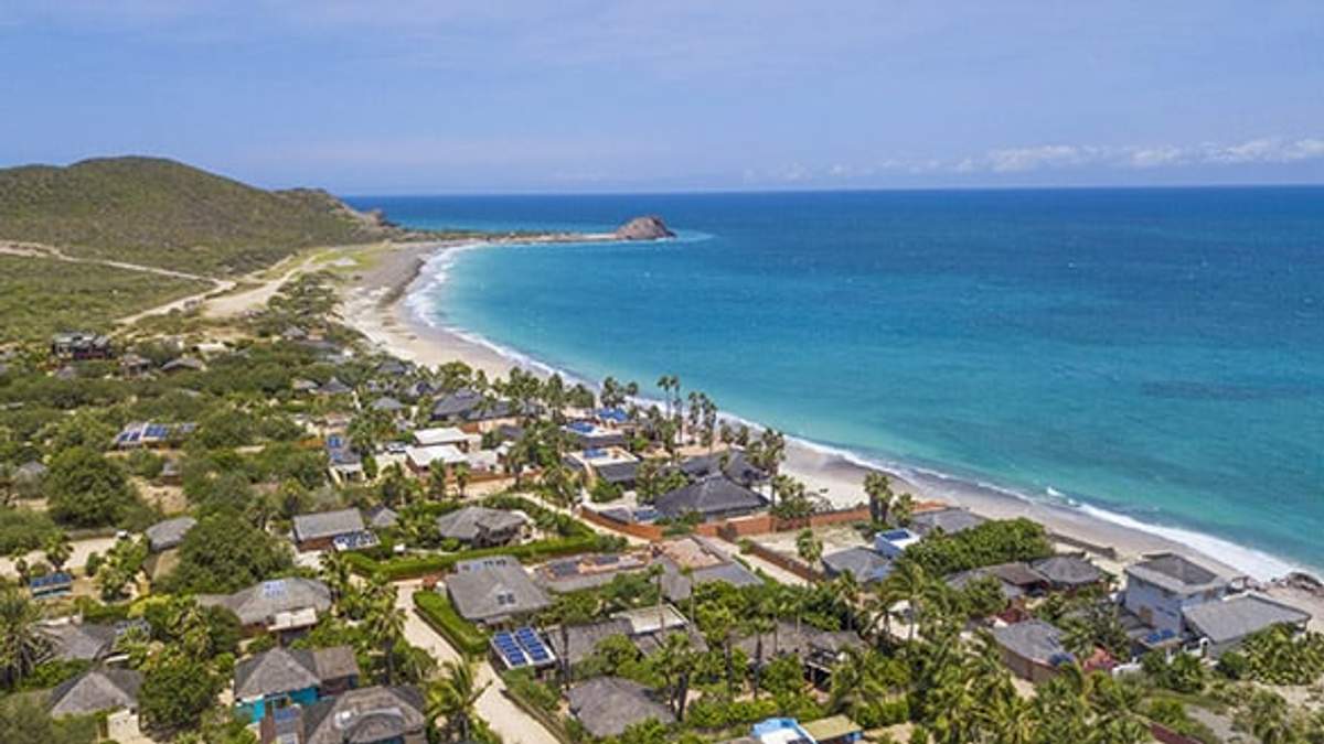 Aerial view of Cabo Pulmo's coastline with houses, lush greenery, and the blue ocean, showcasing its natural beauty and serene environment.