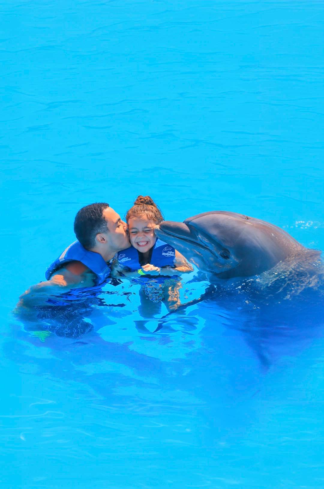 Girl enjoying a dolphin swim experience in Cabo, accompanied by her father.