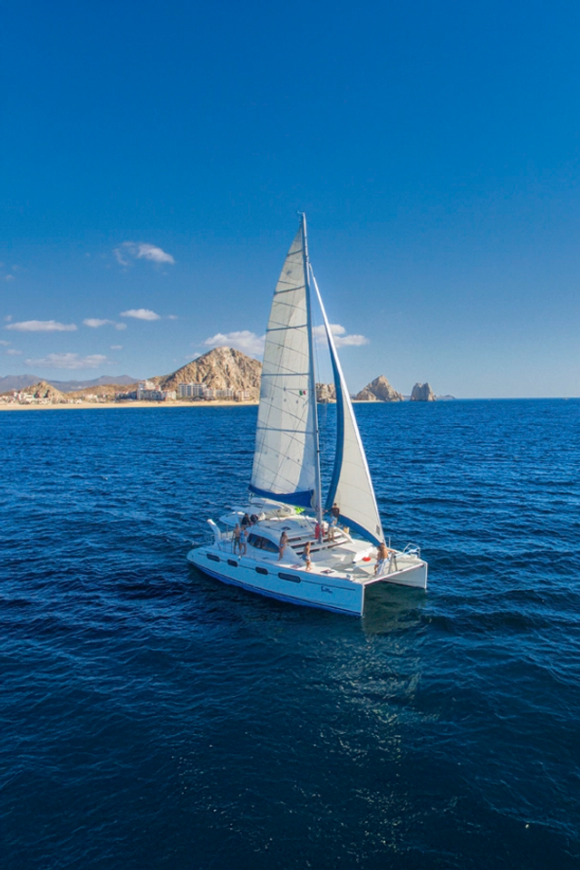 Sailboat cruising past Cabo's iconic arch and rocky formations under a clear blue sky, offering a serene coastal experience.