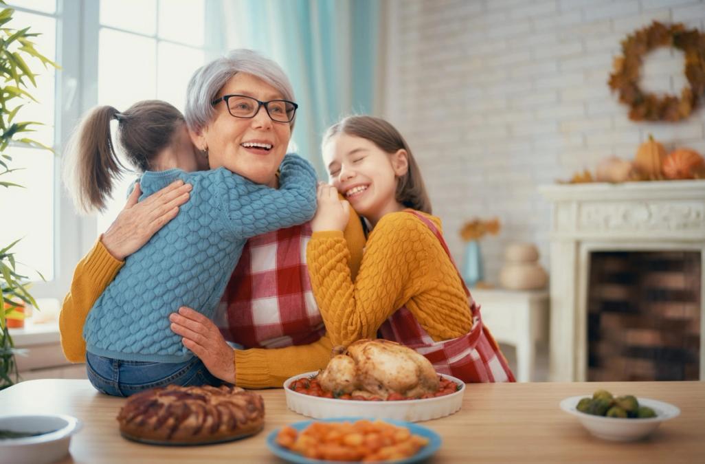 Two young girls hugging their grandmother at the dinner table