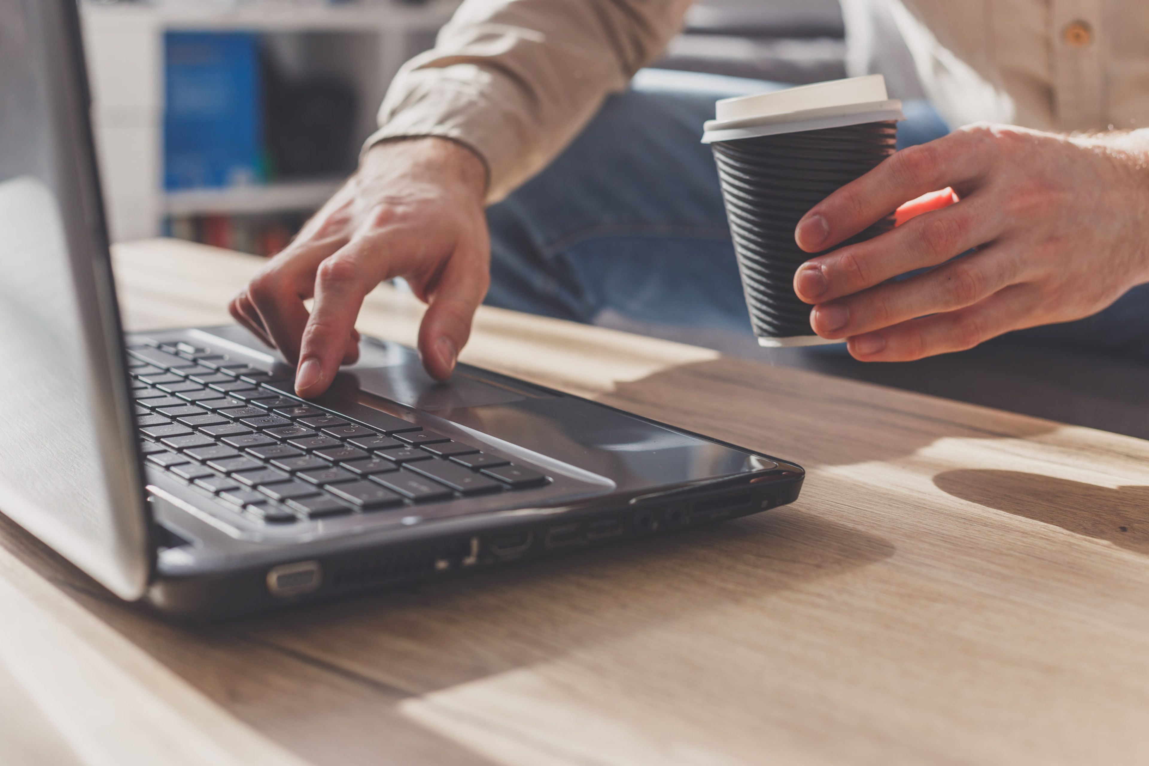 Man holding cup of coffee and typing on laptop with the other