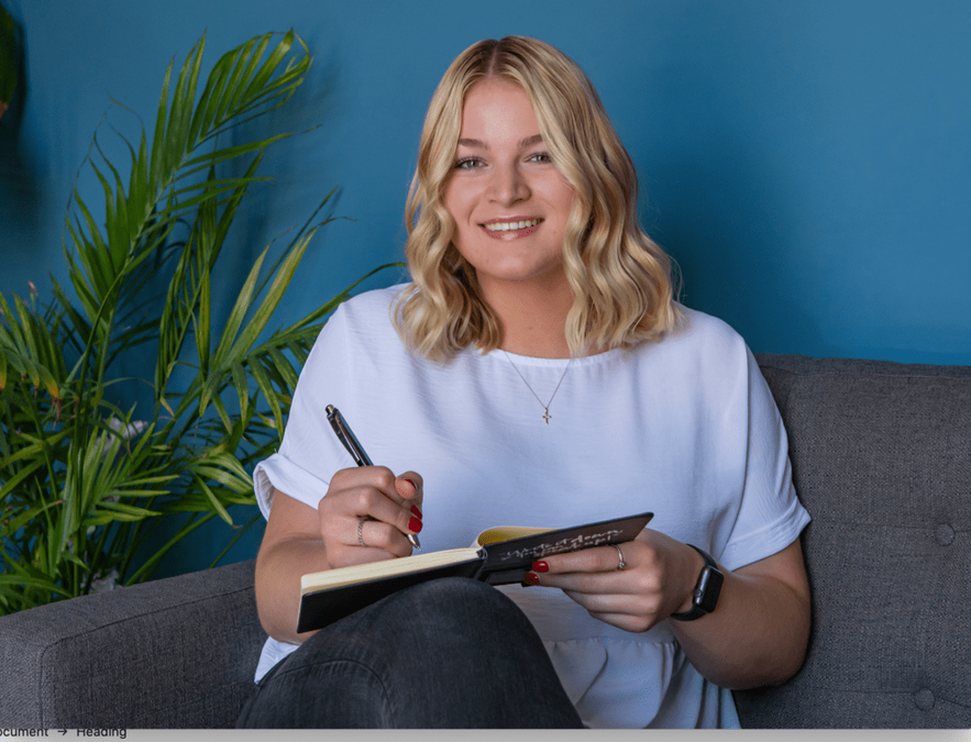 Marketing intern holding journal, smiling while sitting on couch