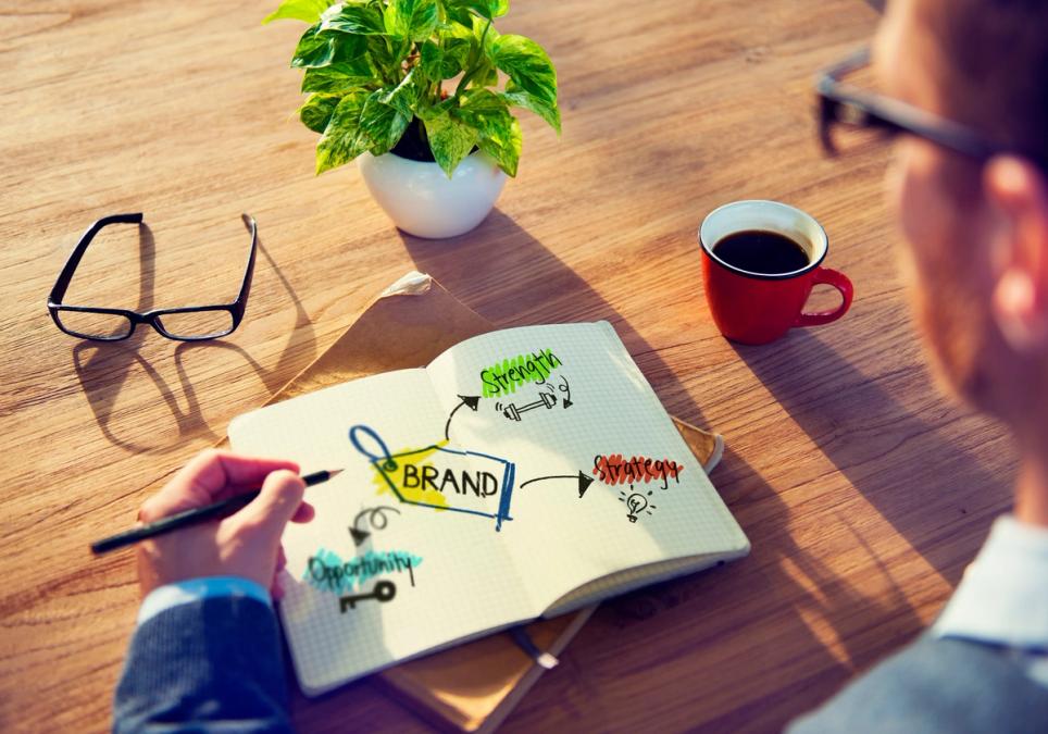 Man looking at notepad with drawings of brand terms, table with glasses and coffee