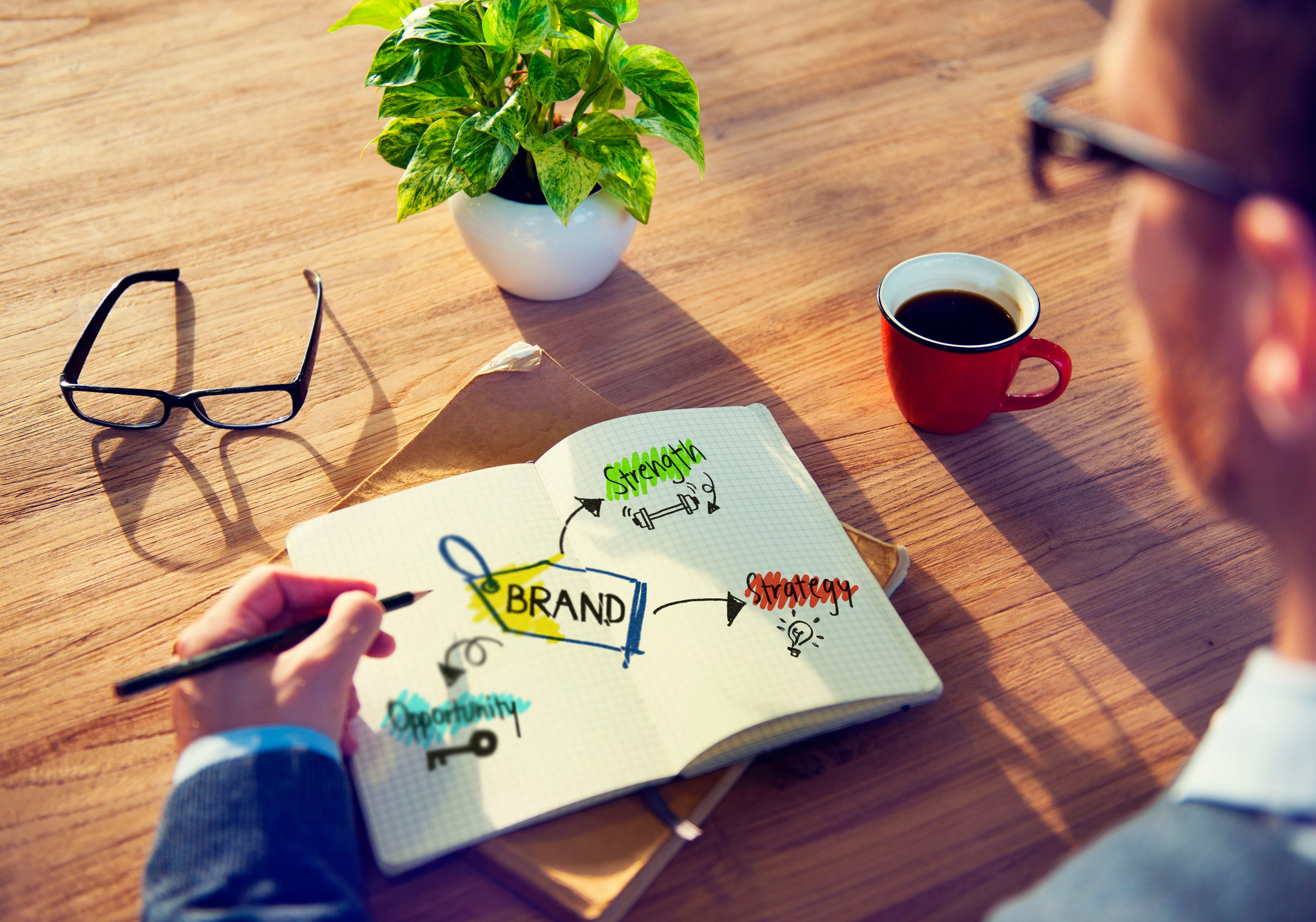 Man looking at notepad with drawings of brand terms, table with glasses and coffee