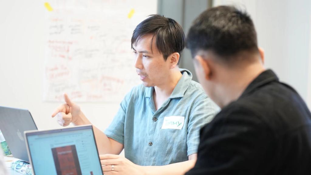 Two participants working through an idea at a whiteboard covered in notes.
