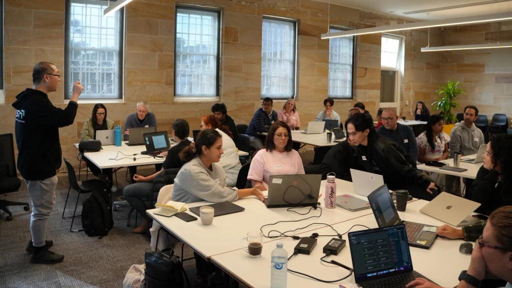 A workshop in progress, participants working on laptops across the room.