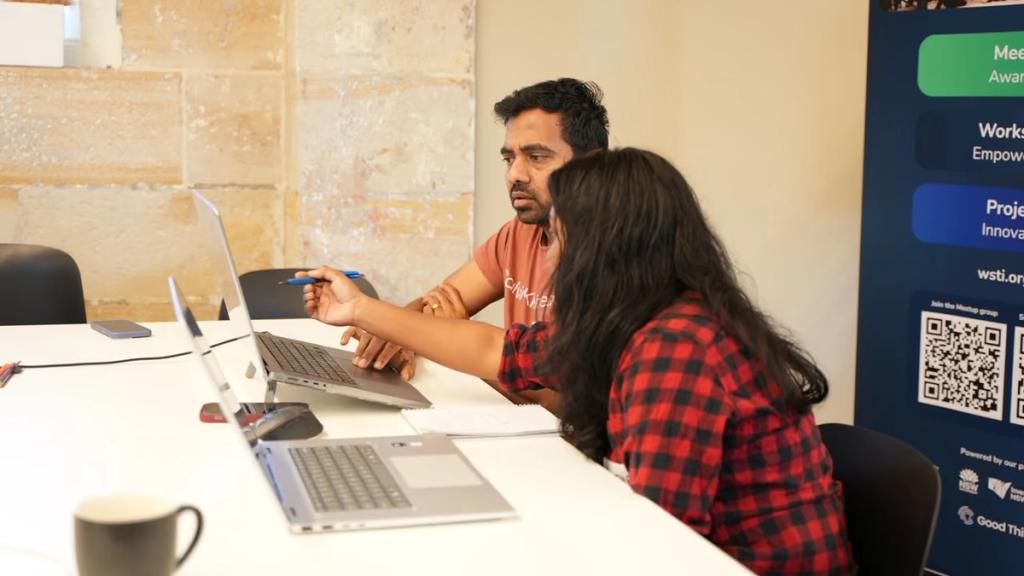 Two builders working at a laptop beside the WSTI banner.