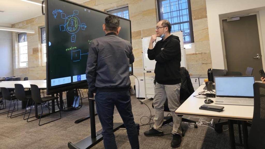 Two people working through a diagram on a whiteboard.