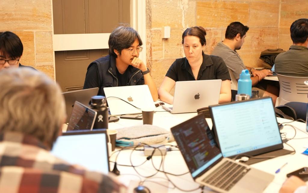 Builders heads-down on laptops at a build session, code up on the screens.