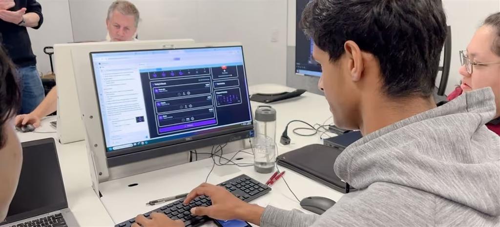 A participant working with AI on a library desktop at an AI Pop In session, others at the table alongside.