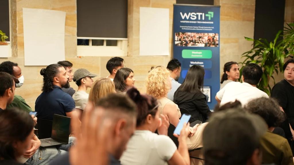 Attendees listening from the back of a packed room.