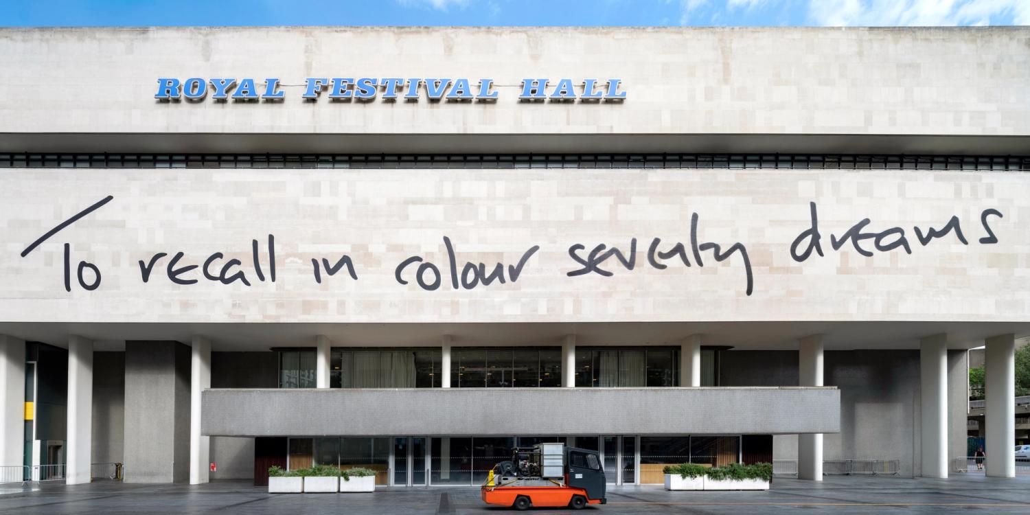 Photograph of a line from a poem printed in handwriting style across the facade of the Royal Festival Hall