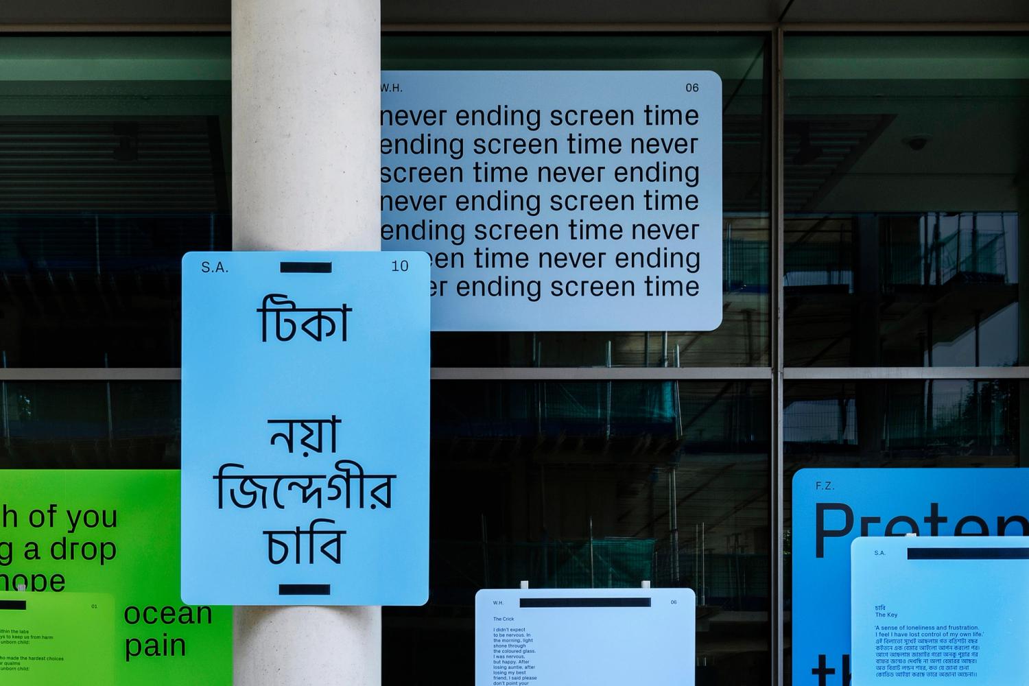 A close-up of a cluster of blue and green panels fixed to windows and columns of a building, with black text printed on them in English and Bengali.