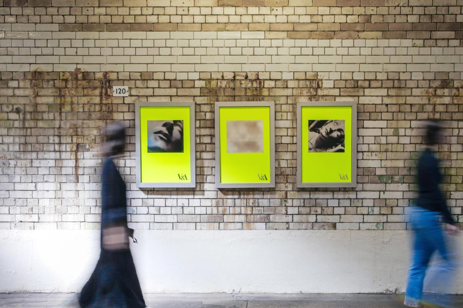 Bright yellow posters with blurred images in subway frames on a brick wall; part of V&A's "Creativity: It's What Makes Us" campaign.