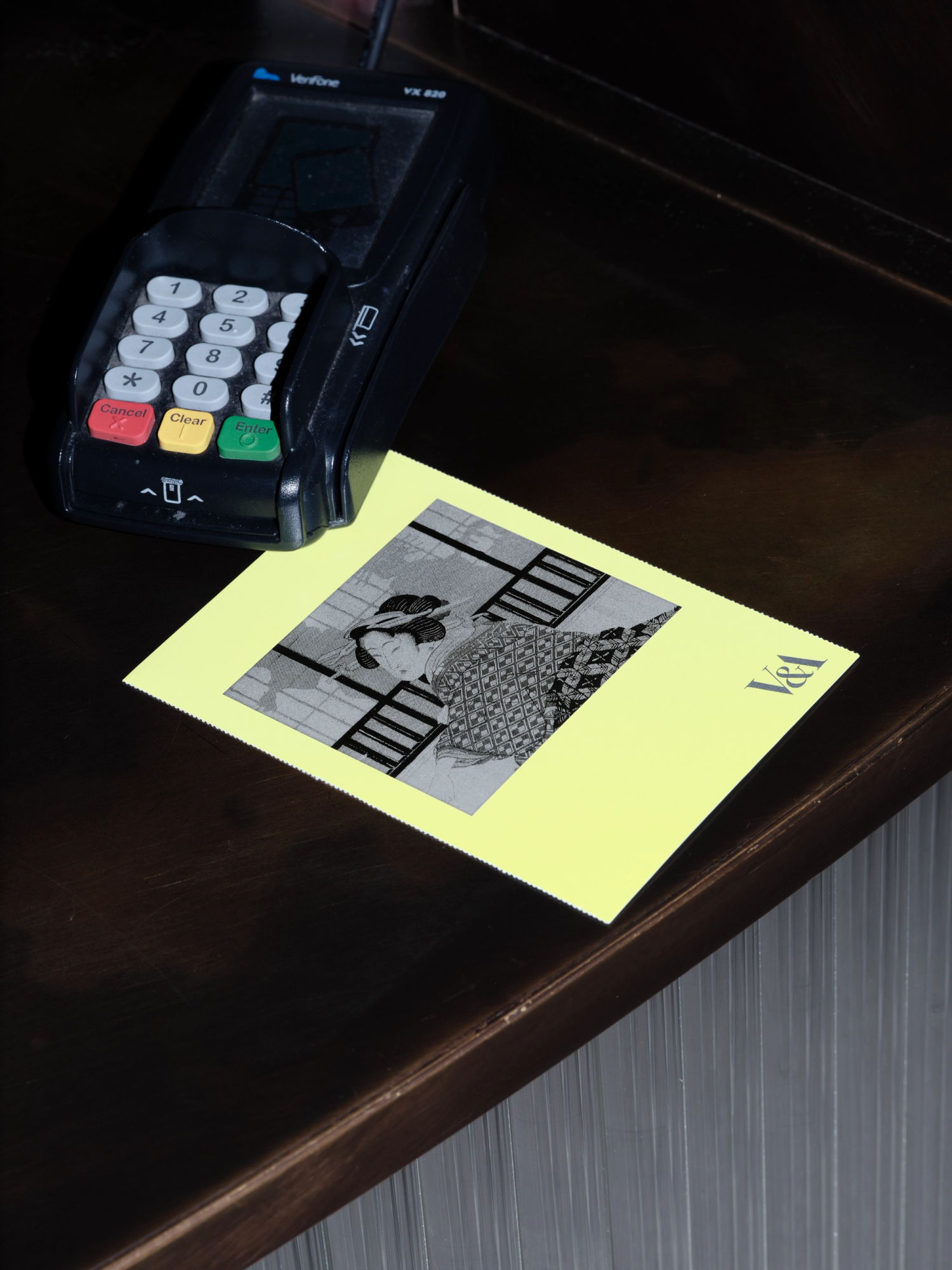 A photograph of a neon yellow booklet with monotone image sat on a counter next to a card machine.