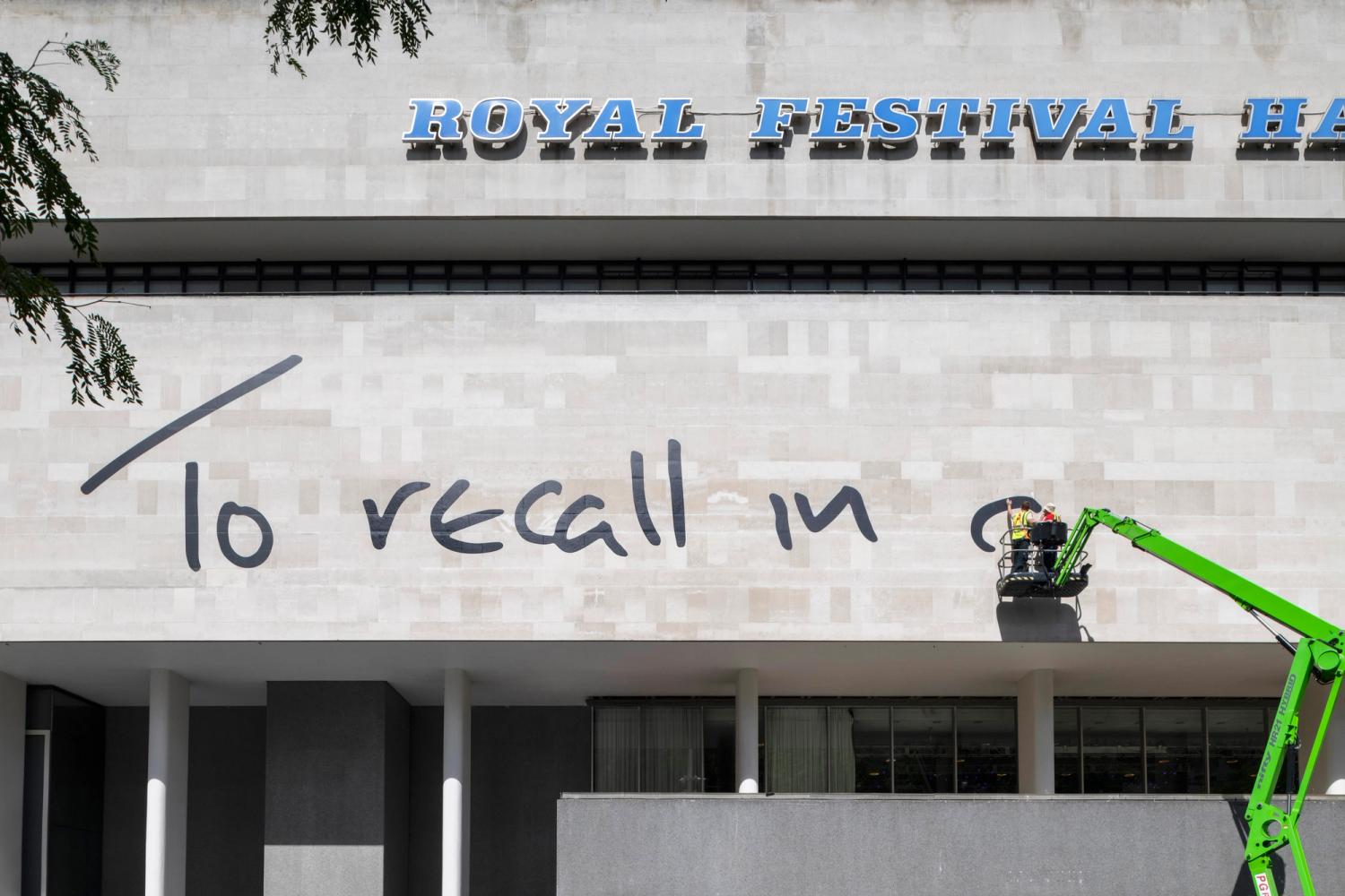Photograph of two men on a green lift installing large text on the facade of the Royal Festival Hall