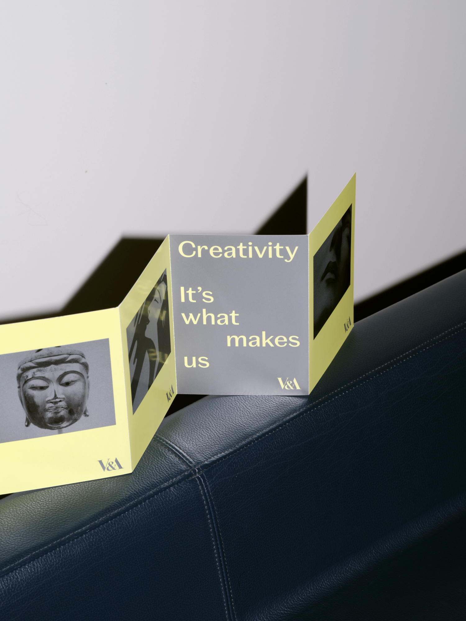 Photograph of a neon yellow and grey concertina leaflet resting on the back of black leather sofa.