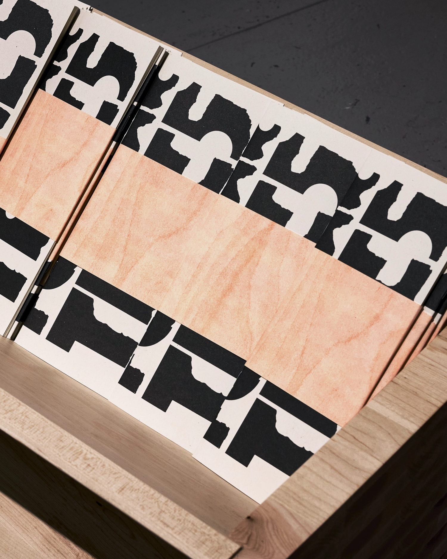 Folded booklets with black-and-white geometric designs and orange belly band sit within a wood container