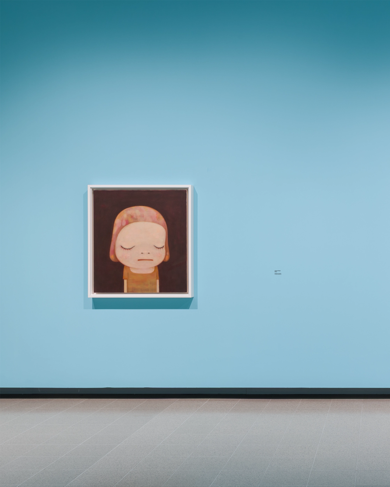An artwork sits framed on a sky blue gallery wall with a caption beside