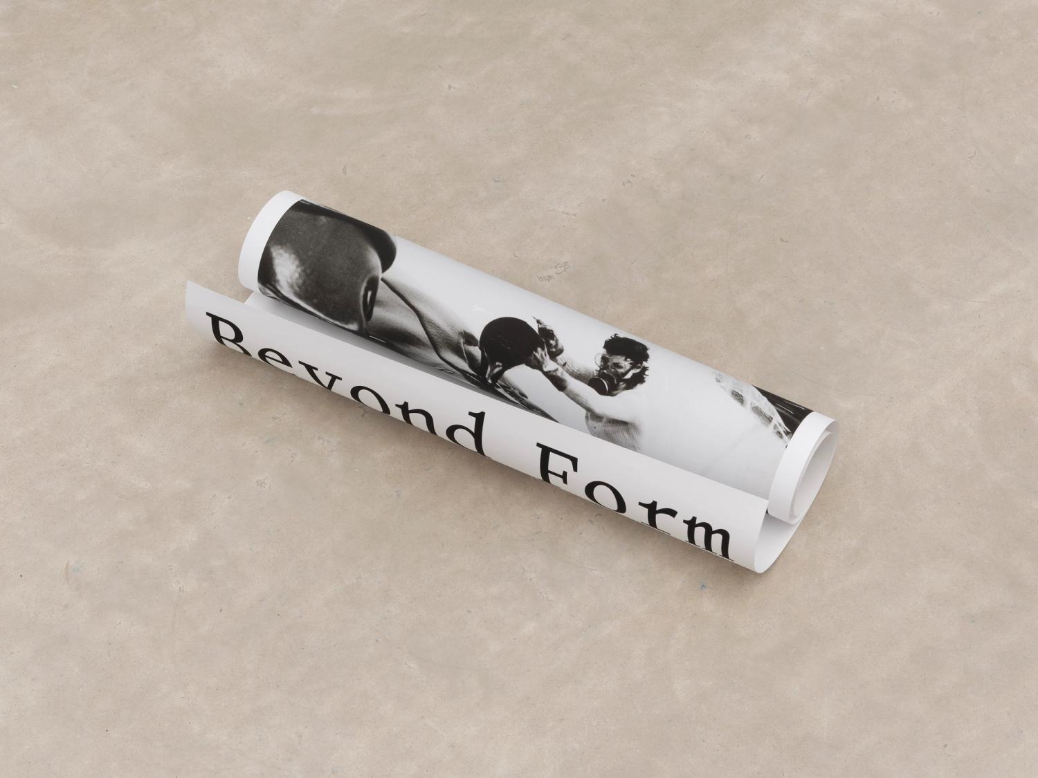 Photograph of Beyond Form exhibition poster, rolled up on concrete floor, showing image of Lynda Benglis