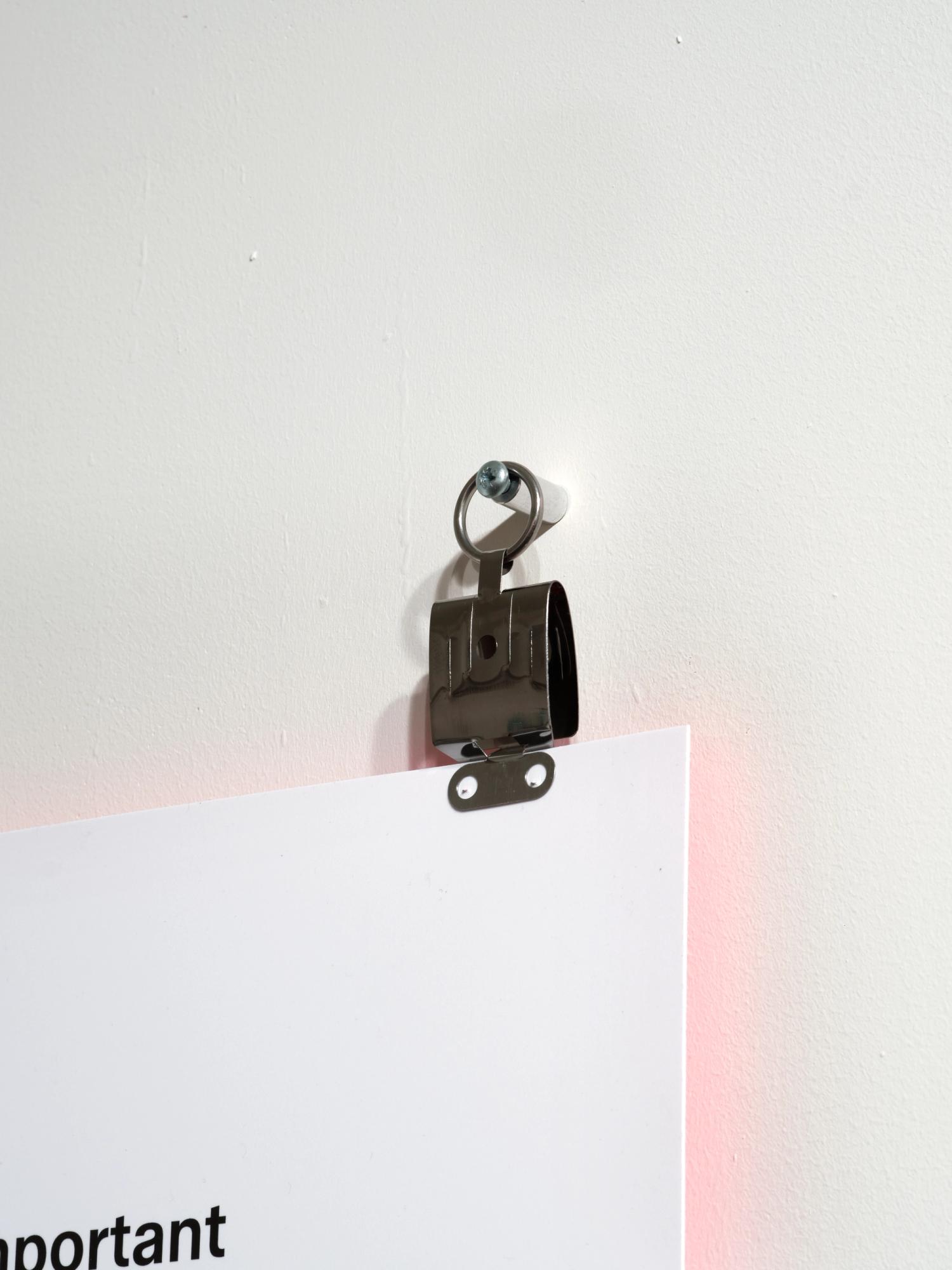 A close-up photograph of a fixing method for a text panel, using large stainless steel photo film clips.
