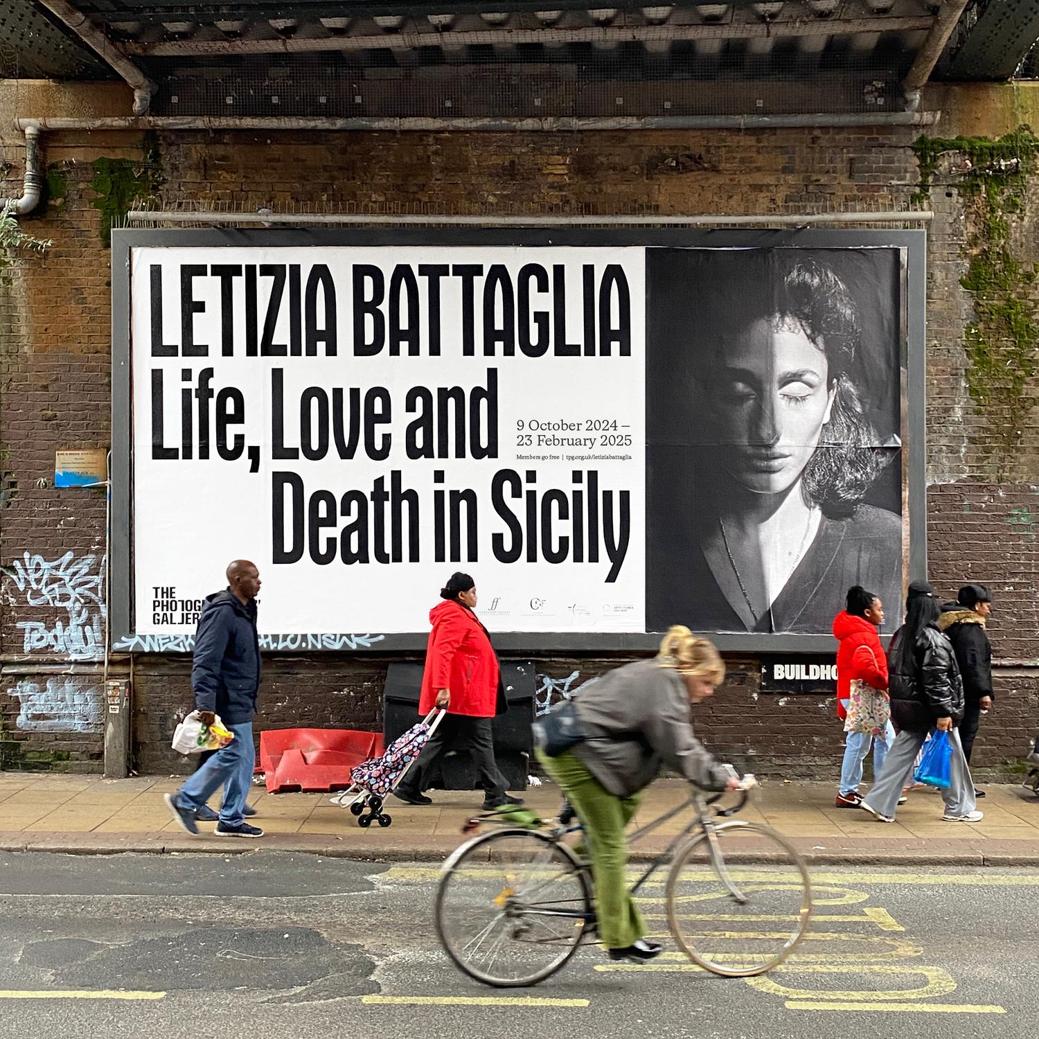 People pass by a billboard with bold type and black and white image of a woman in partial shadow