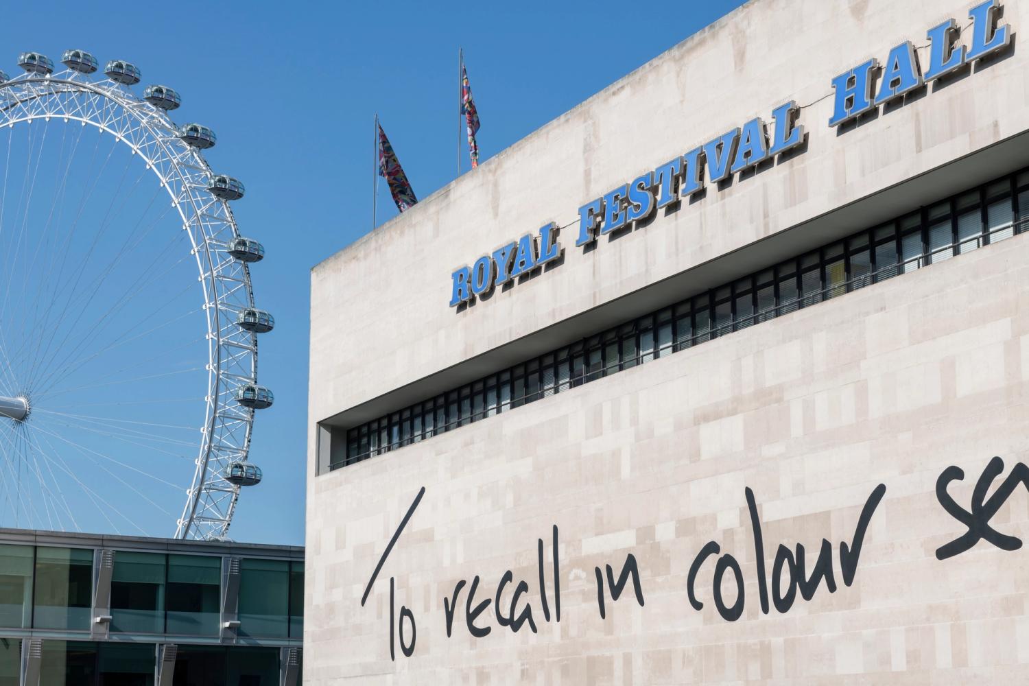 Photograph of large text on the facade of the Royal Festival Hall with London Eye in background