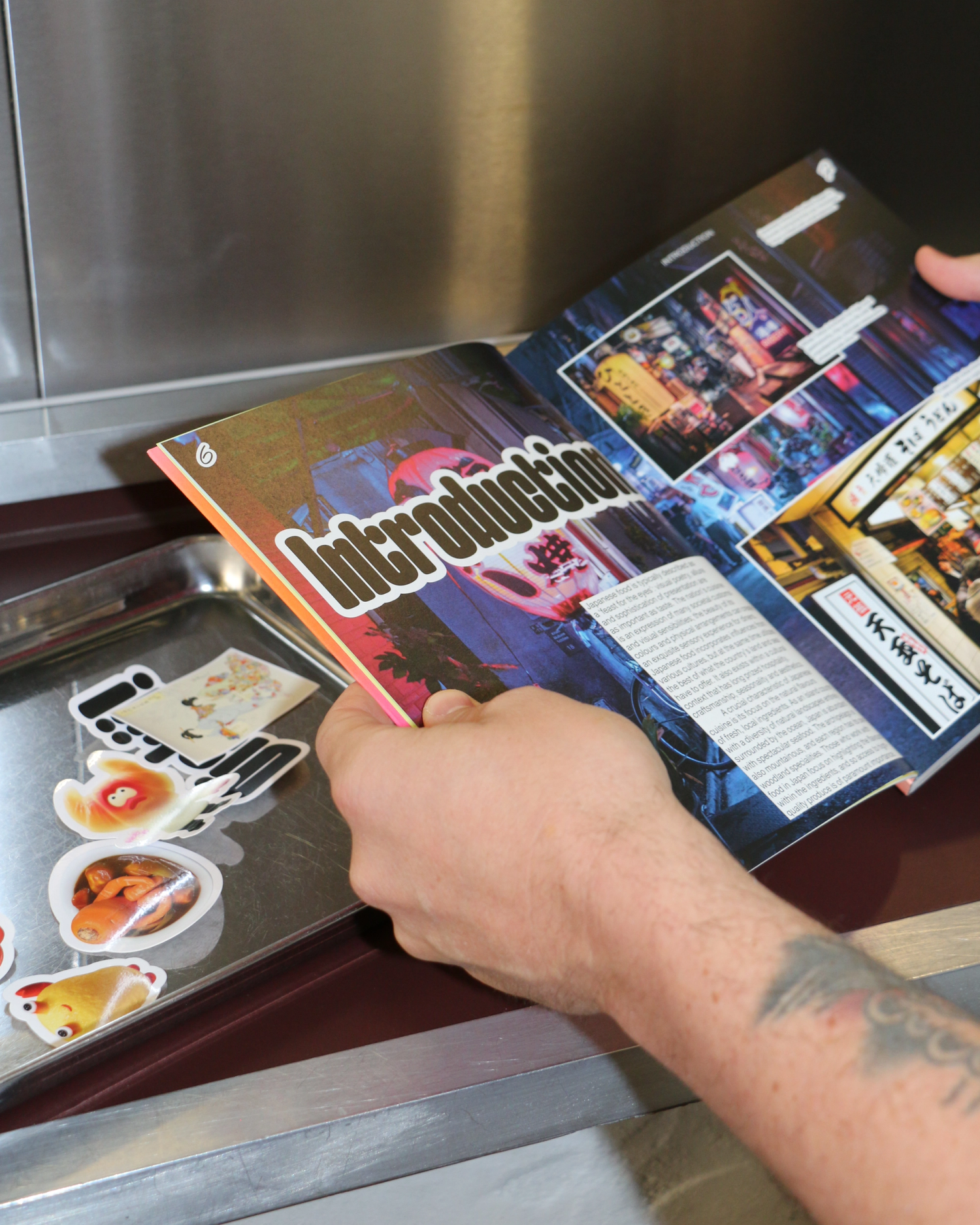 Hands holding a book at a spread that has an image background and the title 'Introduction'. A tray of stickers is beside.