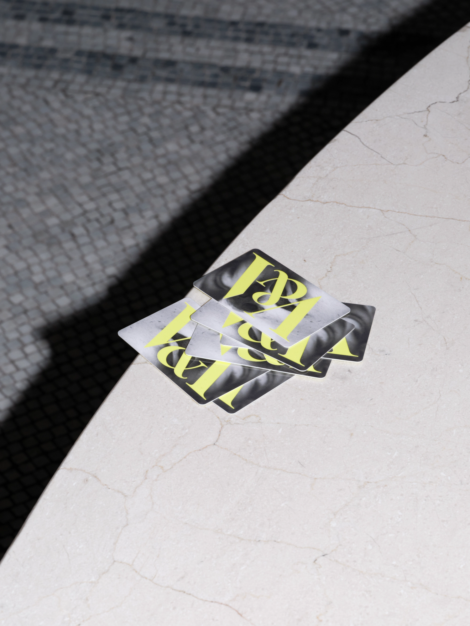 A pile of plastic cards resting on a marble surface. The cards have a monotone image background and neon yellow logo