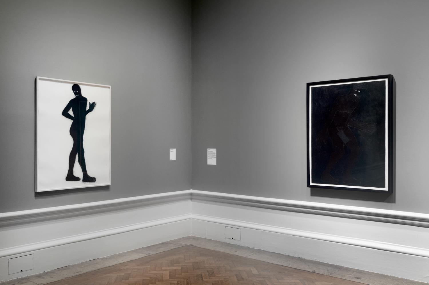 Two artworks on grey walls, featuring dark silhouettes, with captions beside them.
