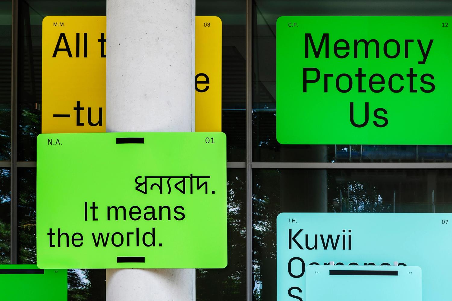 A cluster of yellow, green and blue panels fixed to the exterior of the building. Each panel has text printed, some in English and some in Bengali.