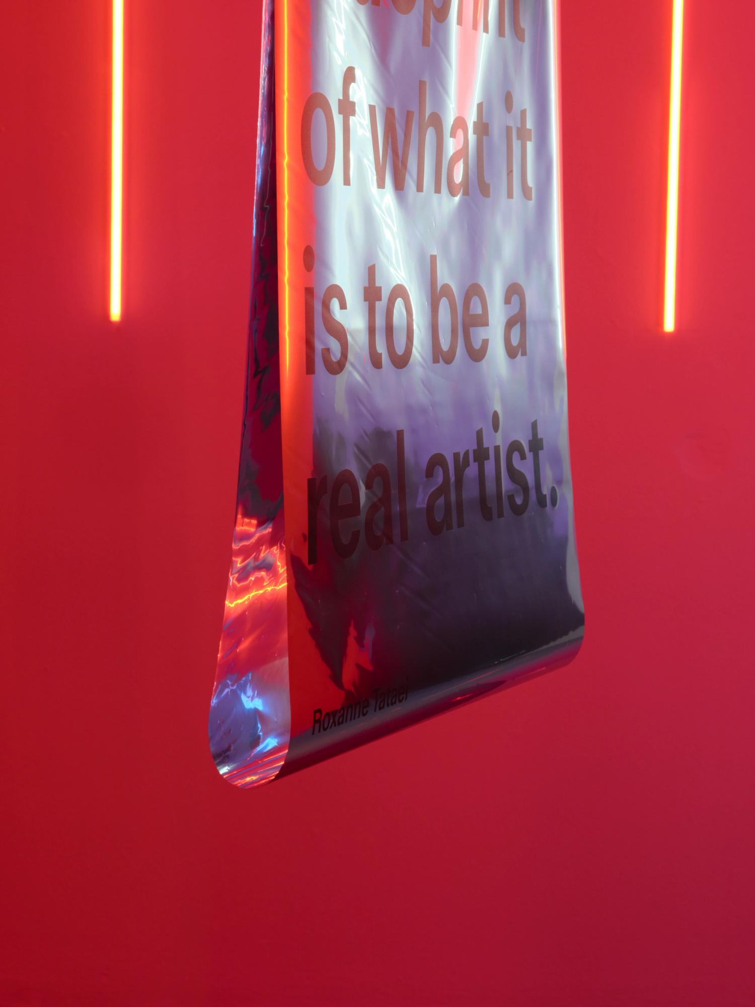 A double sided mylar sheet with text printed to its surface, in an red-lit room.