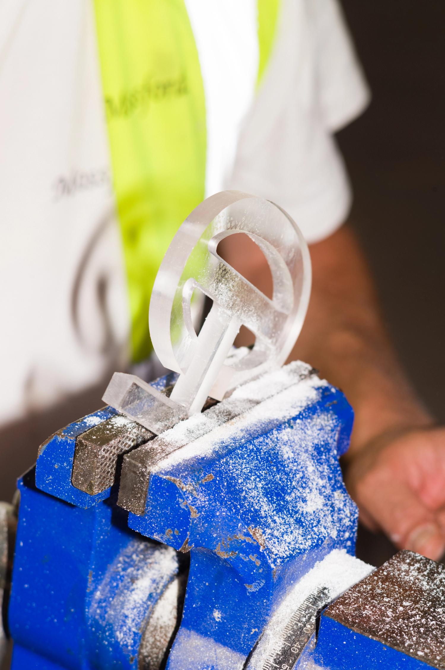 A transparent acrylic letterform clamped in a vice
