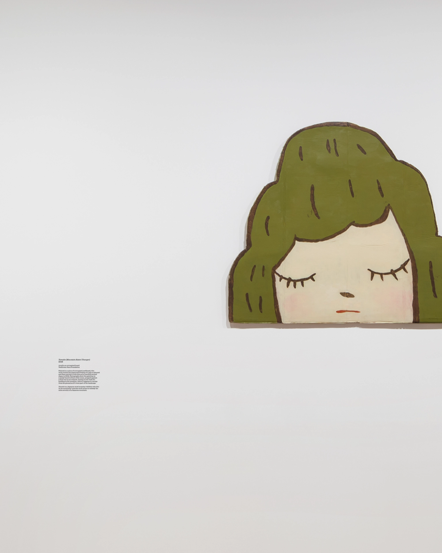 An artwork of a cartoon-style child's head sits on a white wall, with a caption beside