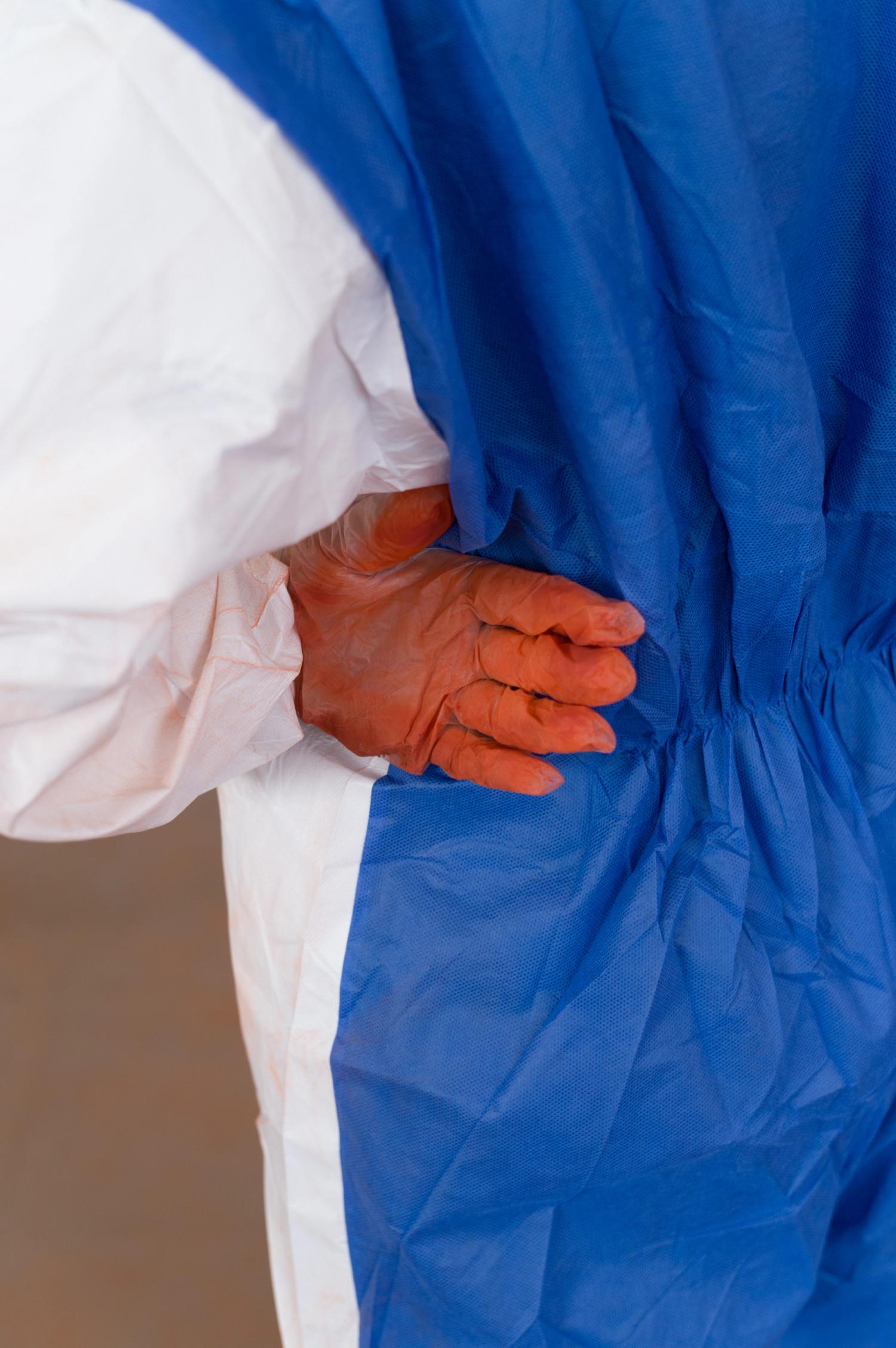 A gloved hand stained red with powder resting on the hip of a person wearing blue and white overalls