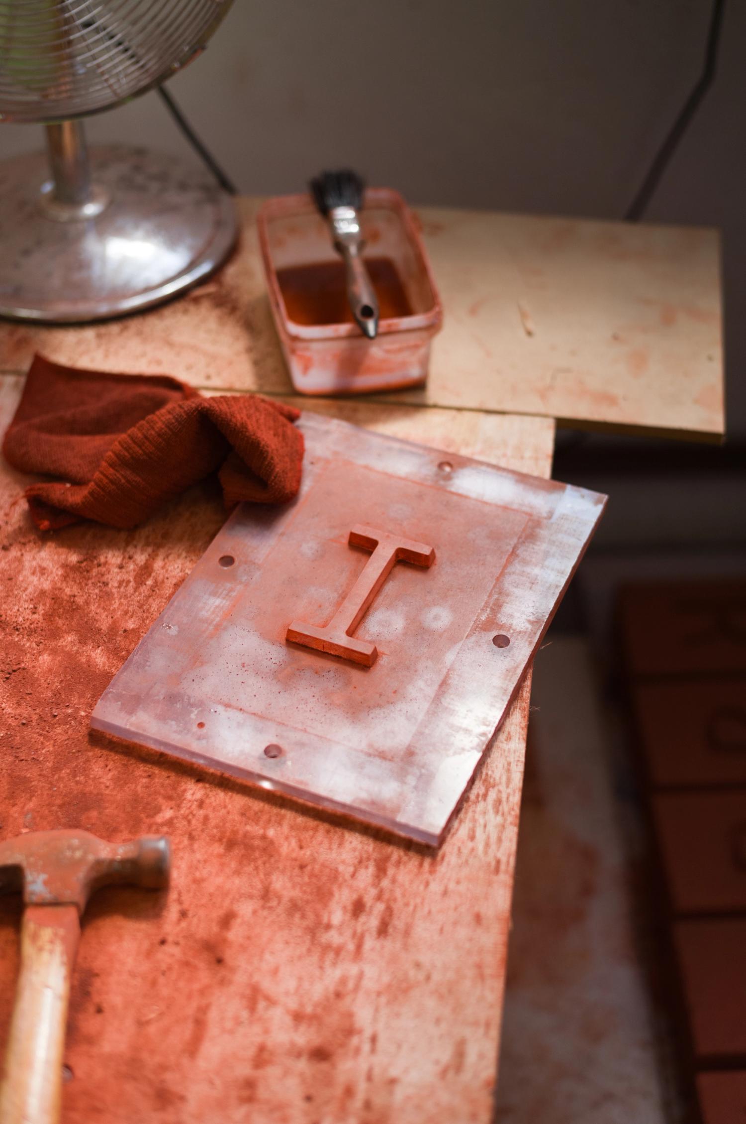 A plastic rectangular plate with protruding letter 'I' on a workbench surrounded by red powder and tools