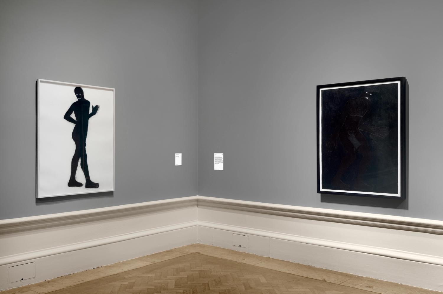 Two artworks on grey walls, featuring dark silhouettes, with captions beside them.