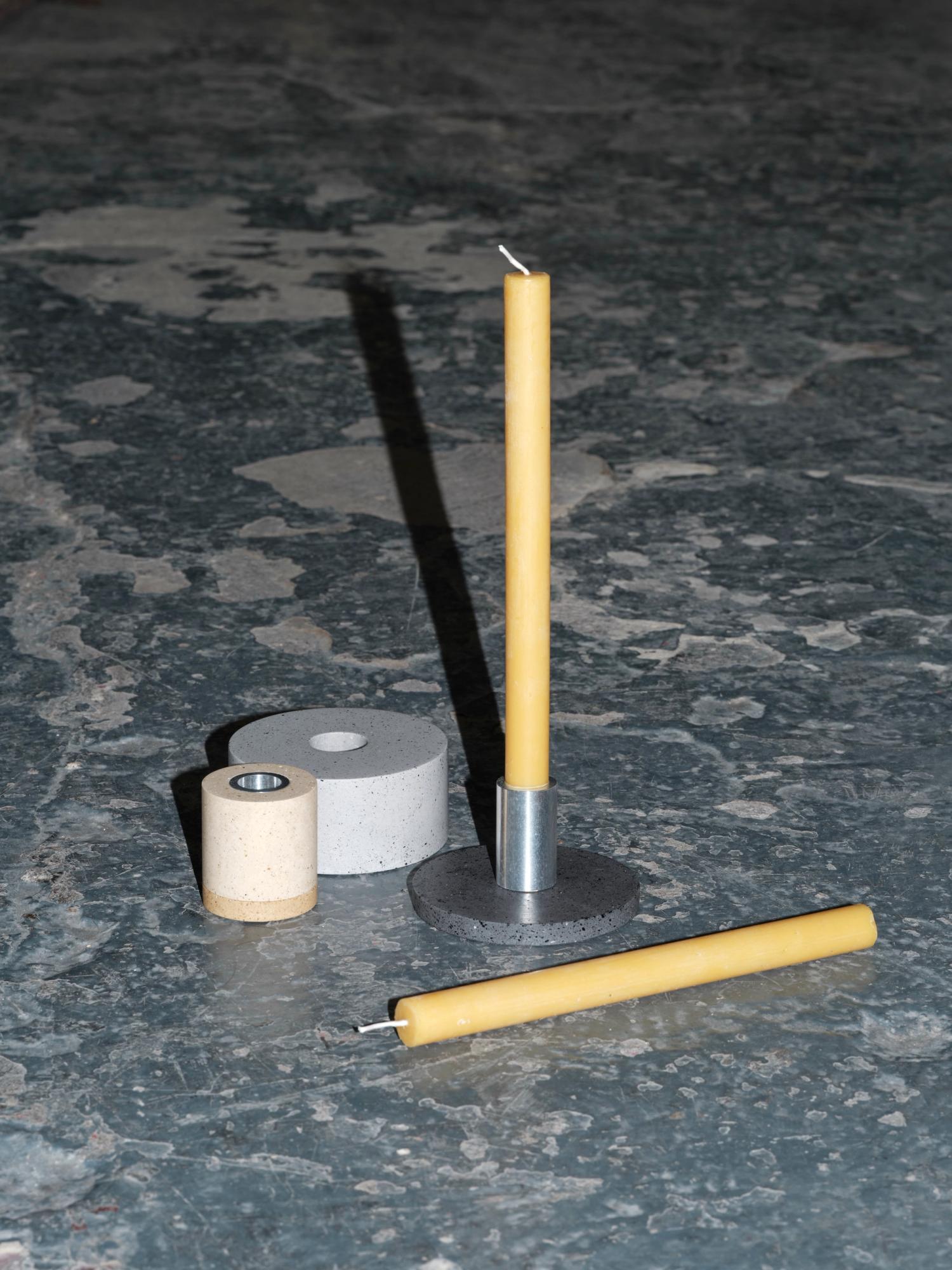 Modular candle holder by Co Projects featuring a yellow candle and concrete and metal components on a textured surface.