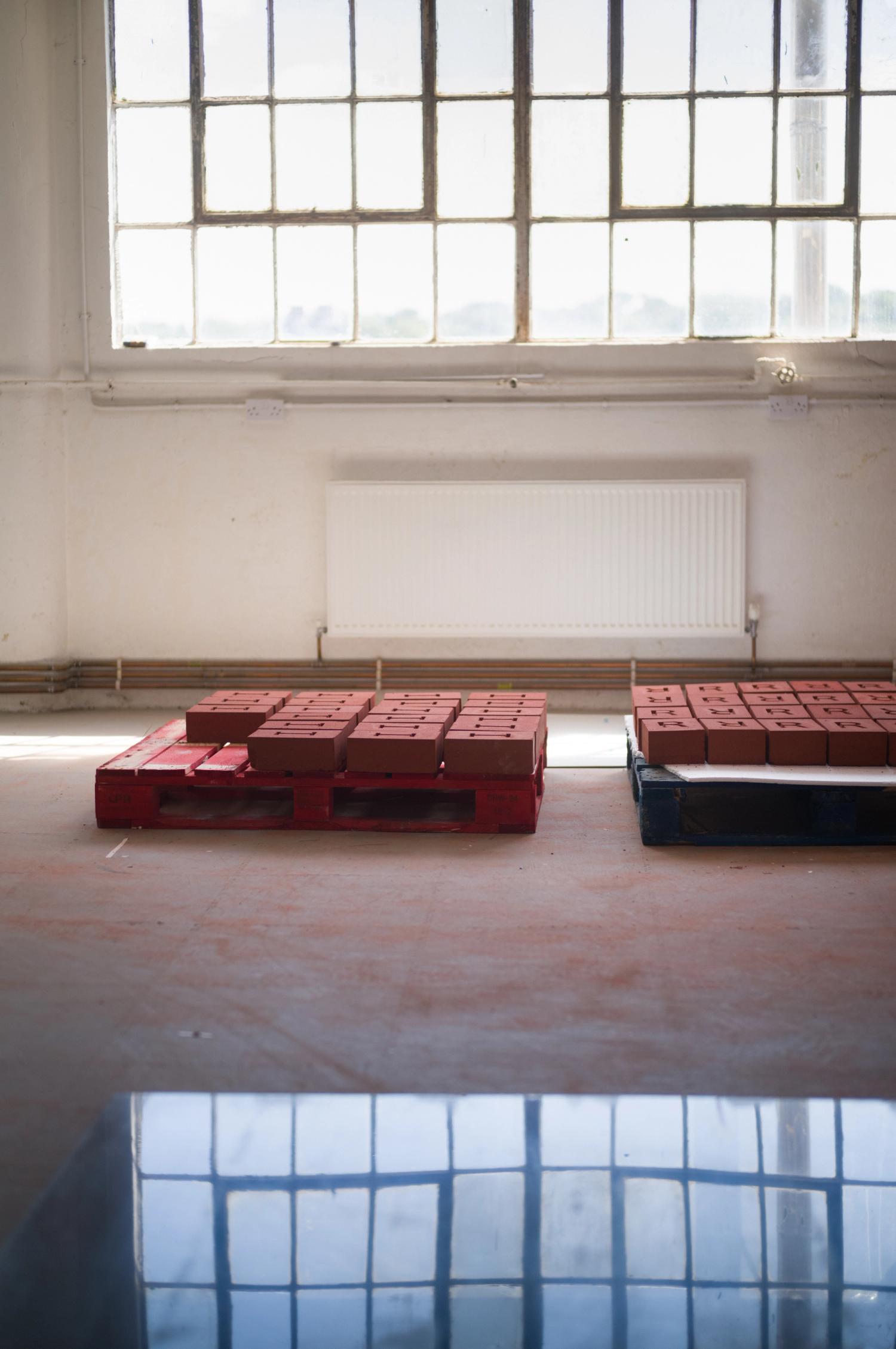 A workshop scene with bricks resting on pallets on the floor under a window