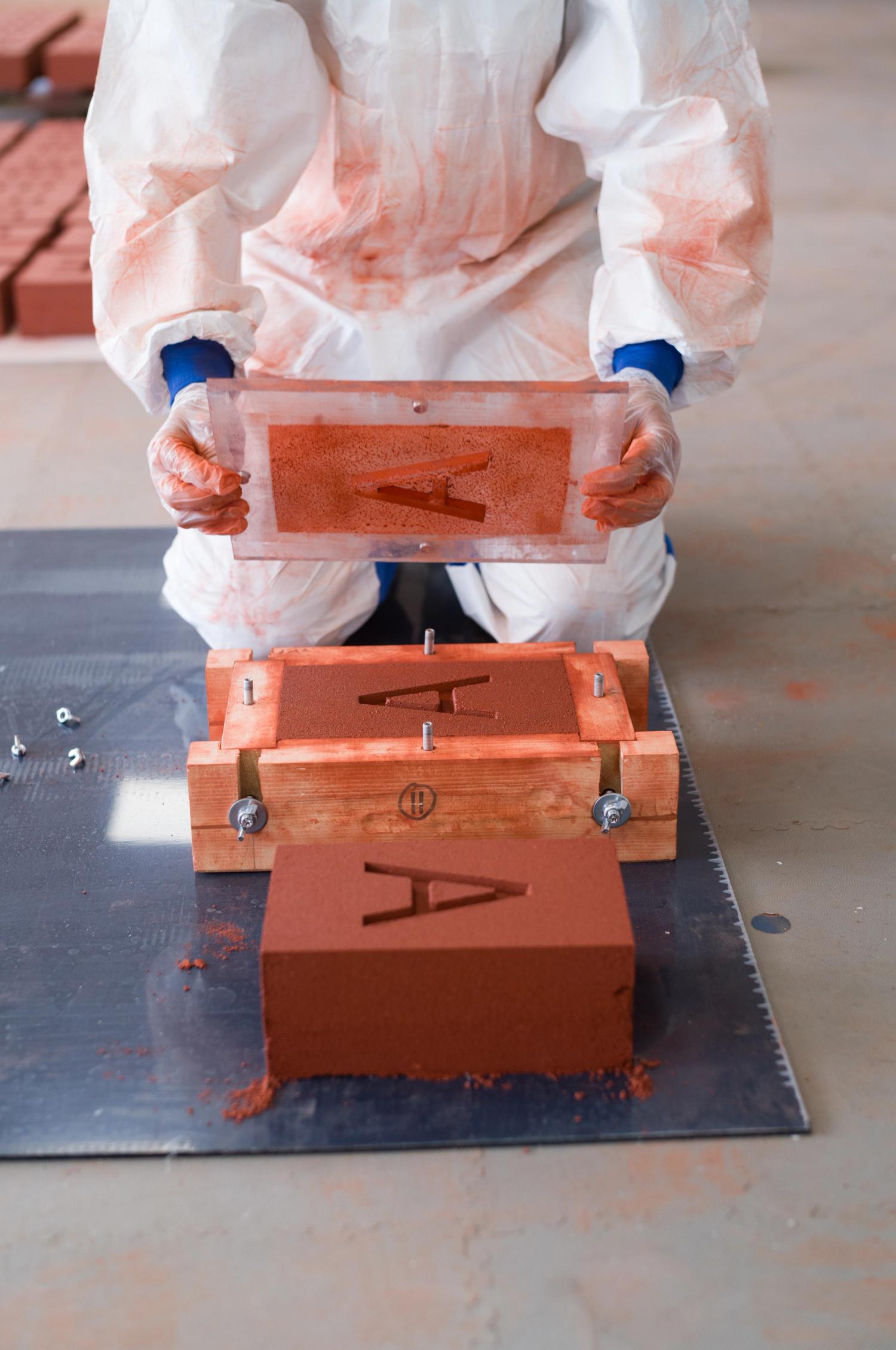 A man in overalls kneeling over a brick in production