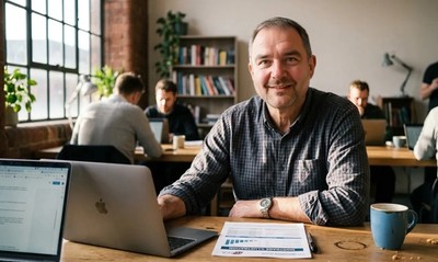 Older man in rolled-up sleeves reviews mortgage paperwork at a sunlit co-working desk in winter.